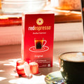 Packung 10 Kapseln redespresso - rooibos espresso auf Holztisch mit Tasse Rooibos Cappuccino